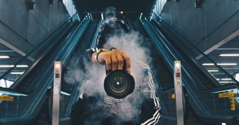 Casual - Man Holding Camera While Squating With Smoke on Face Inside Building