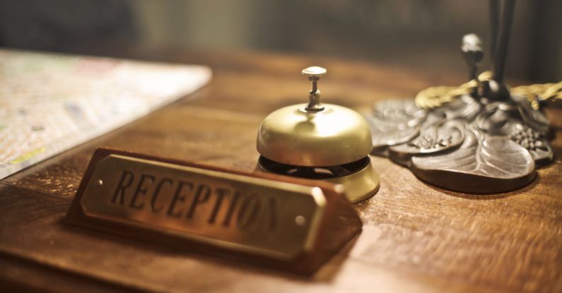 Hospitality - Old fashioned golden service bell and reception sign placed on wooden counter of hotel with retro interior