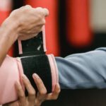 Per Diem - Side view of crop personal trainer preparing African American female for boxing training in gym with punching bags