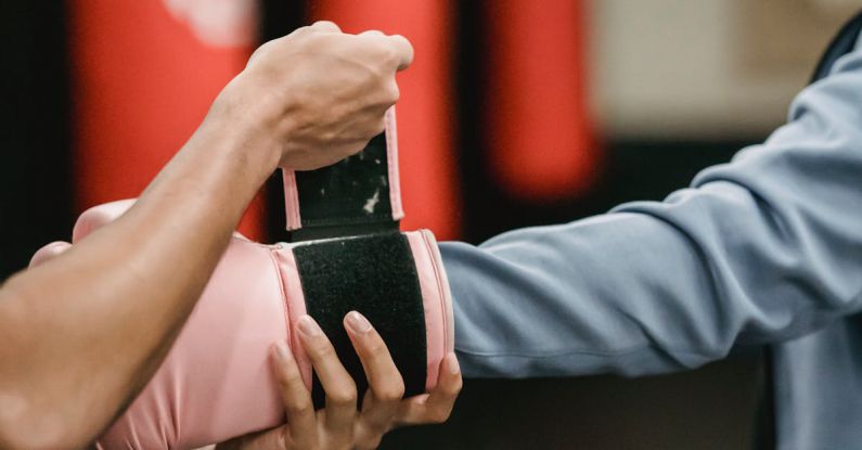 Per Diem - Side view of crop personal trainer preparing African American female for boxing training in gym with punching bags